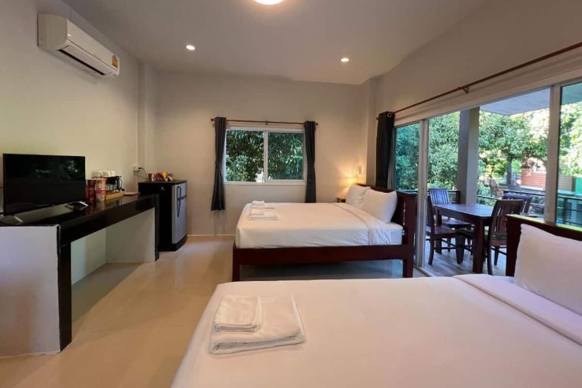 A hotel room with two beds, a desk with a television, and a balcony with a table and chairs.