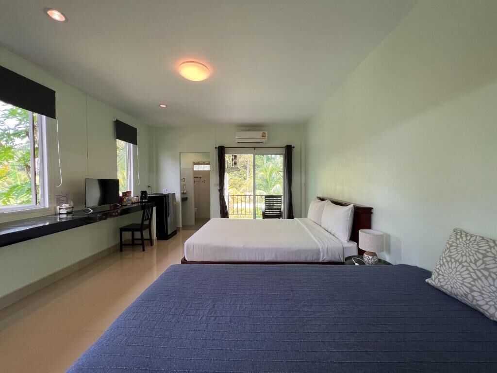 A hotel room with two beds, a desk, a chair, a window, and an air conditioning unit.