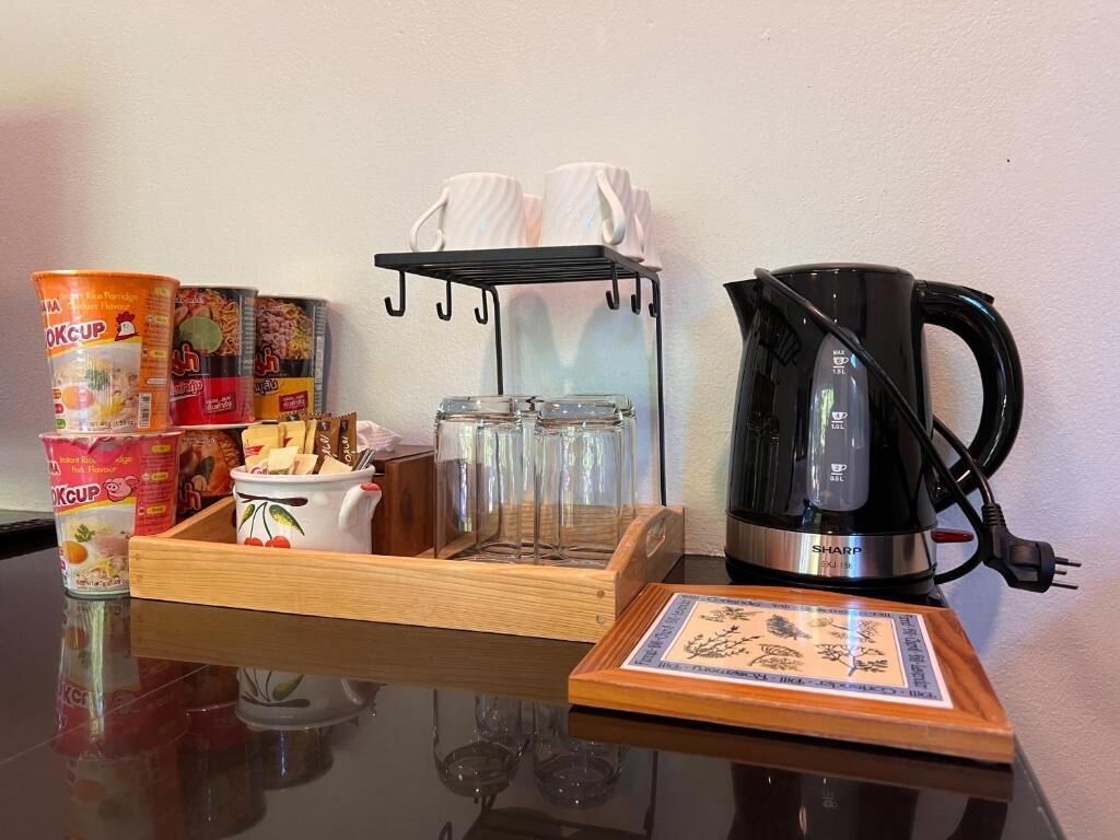 Una mesa con una cafetera, un recipiente con comida, una taza y un asidero para vasos.