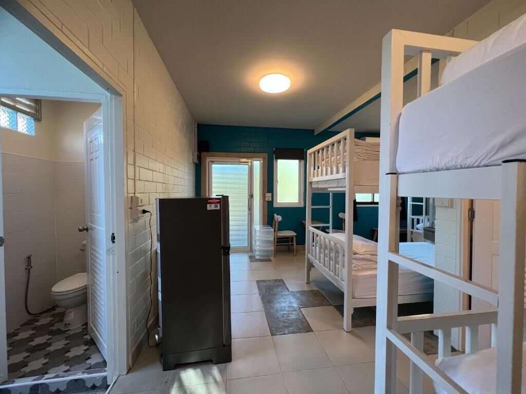 A room with bunk beds, a refrigerator, a door leading to a bathroom, and a window.