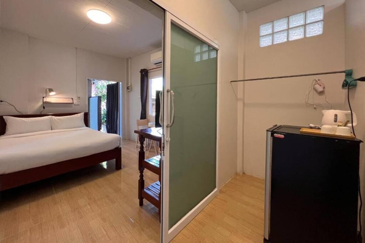 Un dormitorio con cama, escritorio, silla, puerta corredera, ventana y refrigerador.