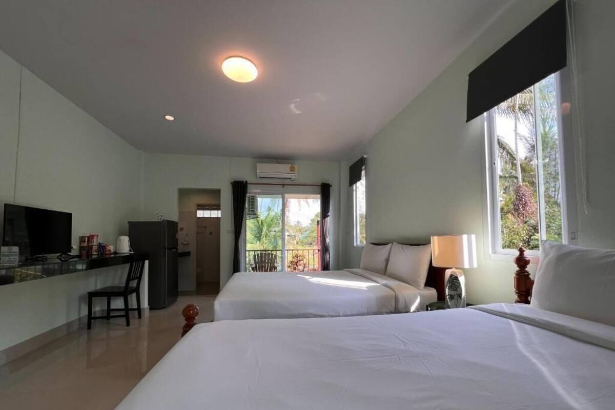 Habitación de hotel con dos camas, un escritorio con televisor, kitchenette y balcón con vistas.