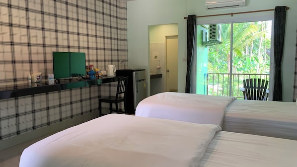 Une chambre d’hôtel avec un mur à carreaux, un balcon donnant sur un paysage verdoyant, deux lits, un petit bureau avec une chaise et un réfrigérateur.