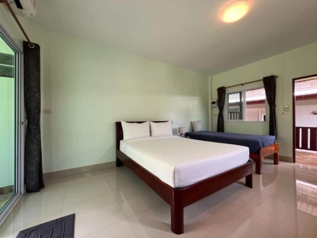 A bedroom with a large bed, a smaller bed, a window with curtains, and a door.