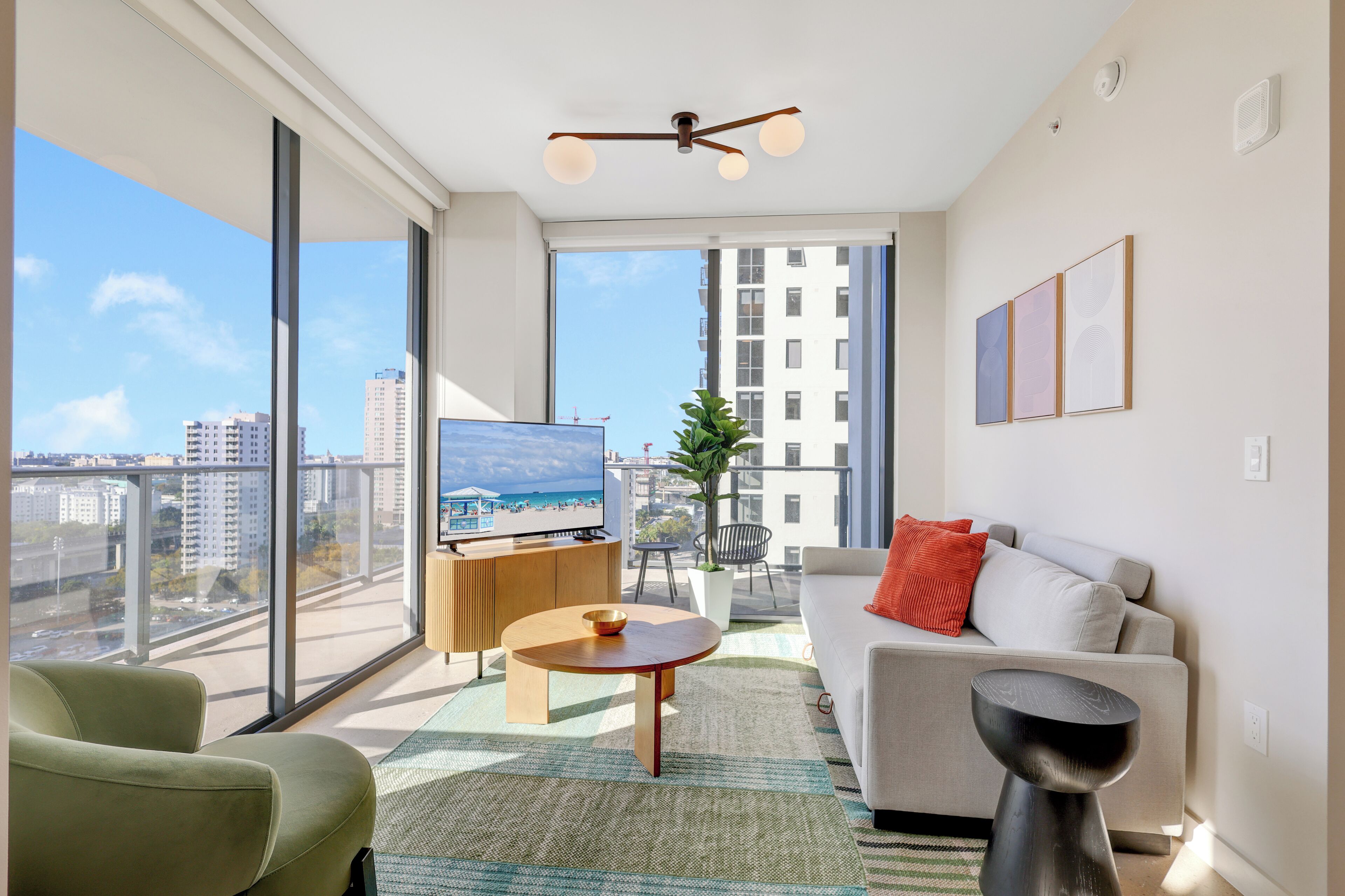 Uma sala de estar moderna com sofá, mesa de centro, TV e varanda com vista para a cidade.