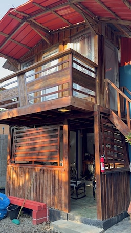 A two-story wooden structure with a balcony, a covered entrance, and a fire extinguisher.. Fresh country air, tranquility, pool, and BBQ—pets welcome.
