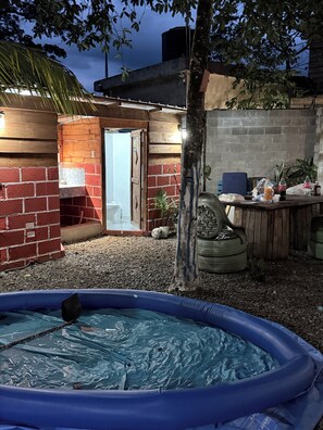 An outdoor patio area with a brick wall, a wooden door, a small seating area, and an inflatable pool. - Fresh country air, tranquility, pool, and BBQ—pets welcome. (Bonao)
