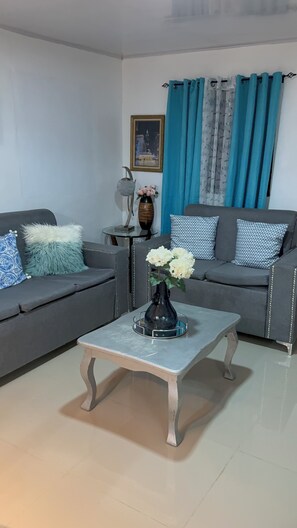 A living room with two grey sofas, a small table with a vase of flowers, and a framed picture on the wall.