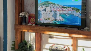 A television mounted on a wooden shelf with a marble wall backdrop, potted plants, and a ceiling with exposed beams. - Fresh country air, tranquility, pool, and BBQ—pets welcome. (Bonao)