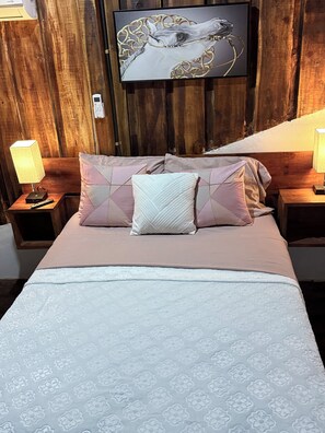 A bed with a patterned bedspread, two nightstands with lamps, a wall-mounted TV, and a wooden headboard.