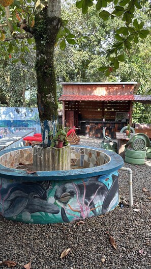 A rustic outdoor seating area with a mosaic pool, wooden tables, and a rustic building with a tiled roof. - Fresh country air, tranquility, pool, and BBQ—pets welcome. (Bonao)