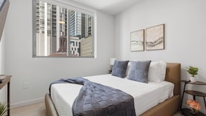 A modern bedroom with a large bed, a window with a city view, and two framed artworks on the wall. - AEA - 121 NE 5th St Miami (Miami)