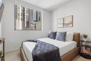A modern bedroom with a large bed, a window with a city view, and two framed artworks on the wall. - AEA - 121 NE 5th St Miami (Miami)