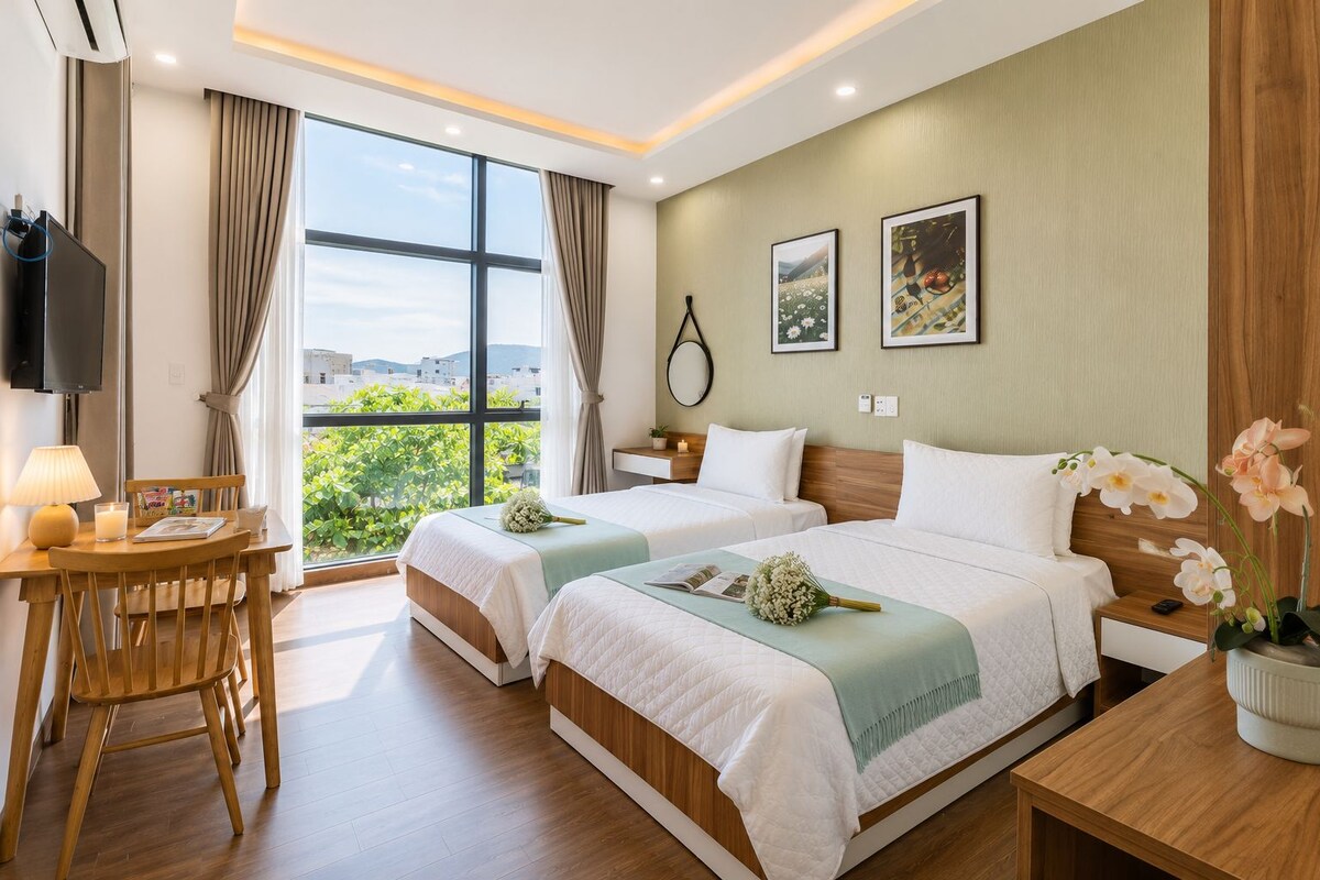 A hotel room with two beds, a desk, a chair, a TV, and a large window with a view.