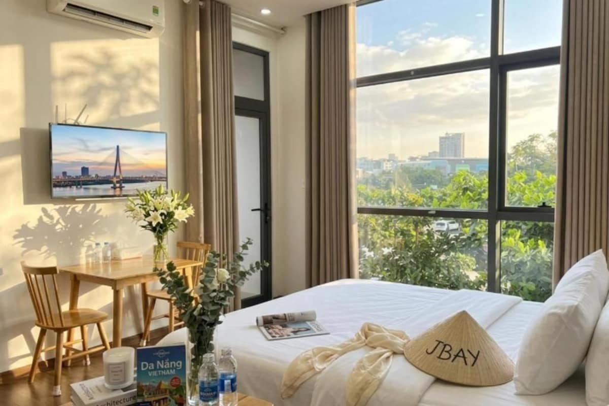 A hotel room with a bed, a desk, a chair, a TV, and a window with a city view.