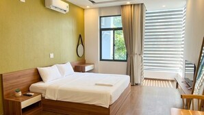 A hotel room with a wooden bed, a bedside table with a remote control, a small plant, and a window with curtains. - JBAY Riverfront Boutique Hotel (Da Nang)