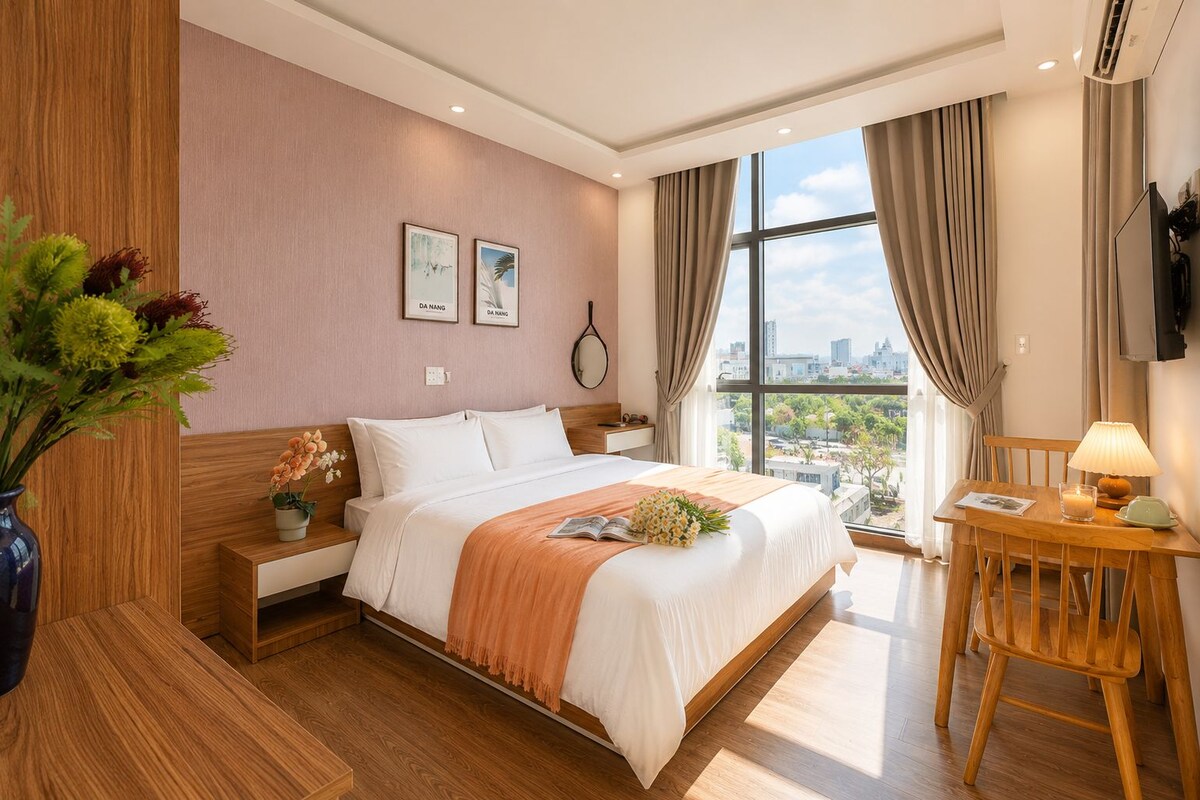 A hotel room with a bed, bedside table, lamp, and a view of the city through large windows.