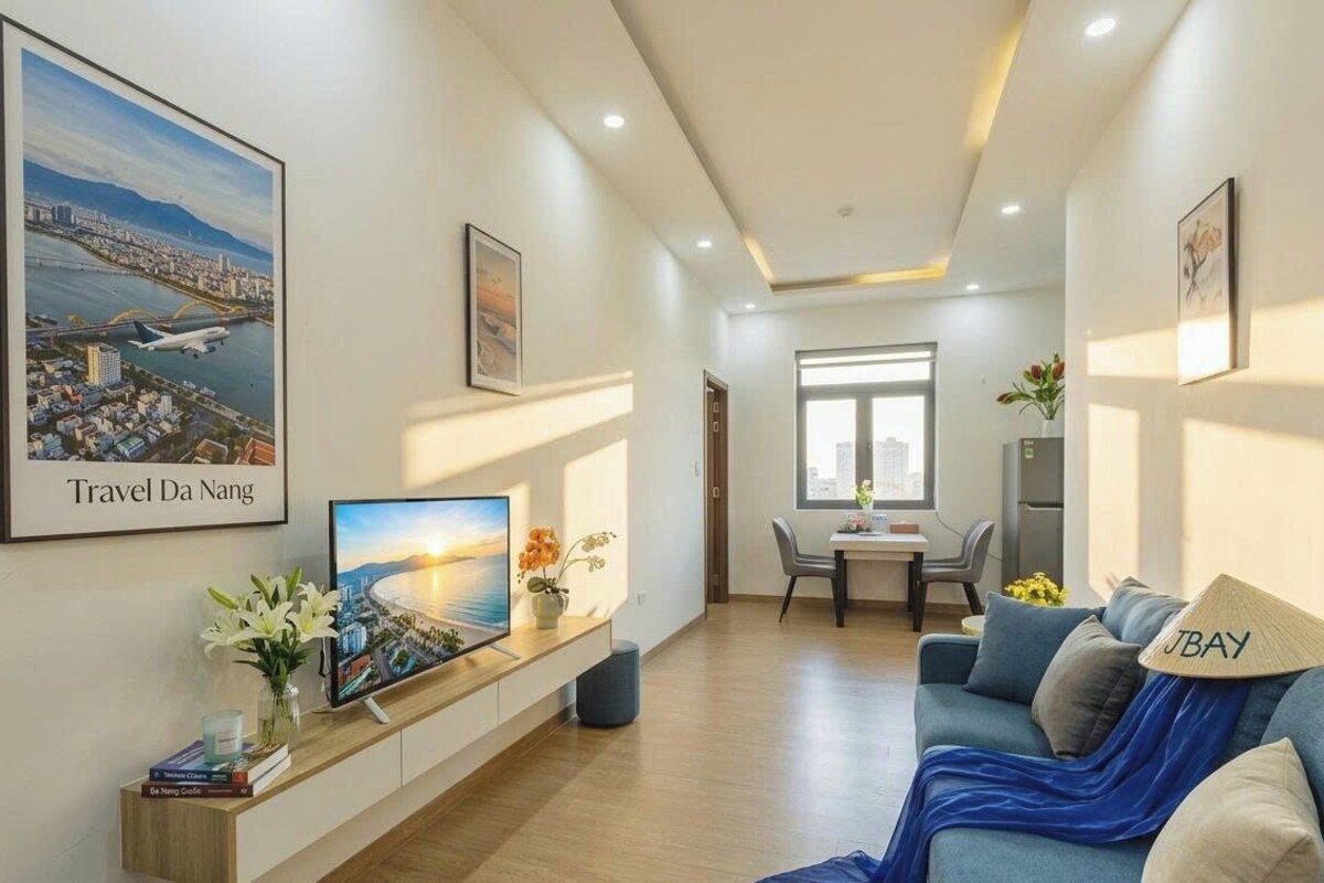 A modern hotel room with a large TV, a sofa, a dining area, and a cityscape view.