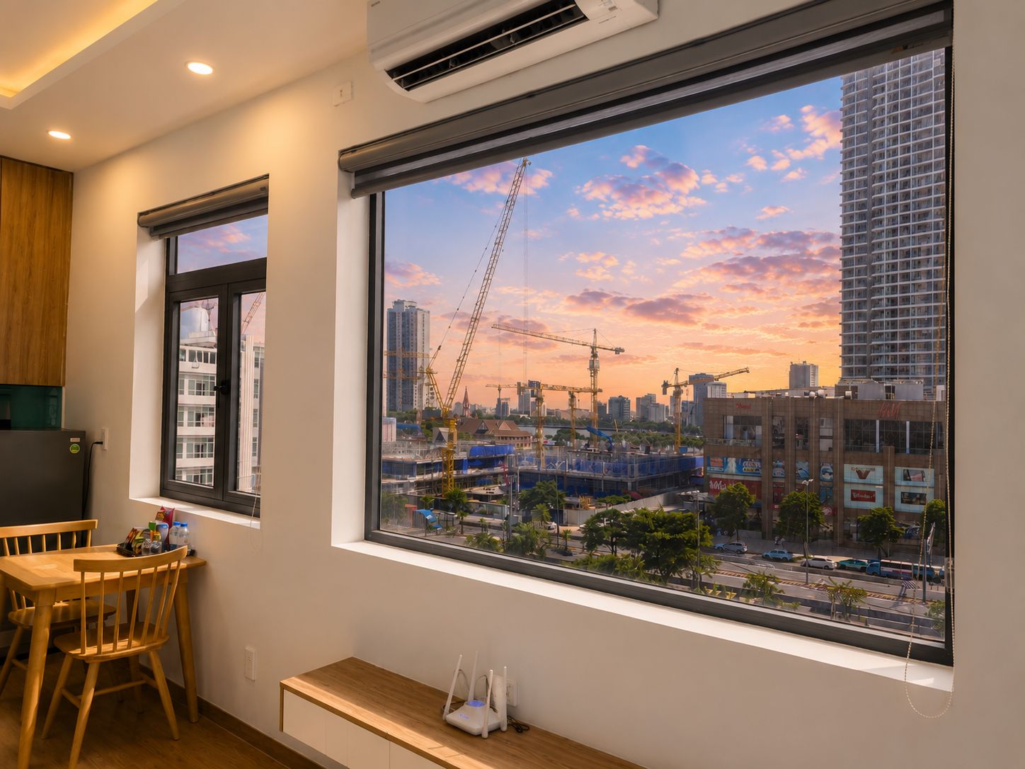 A room with a large window overlooking a construction site and a cityscape at sunset.