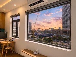 Ein Zimmer mit großem Fenster, das einen Blick auf eine Baustelle und die Skyline im Sonnenuntergang bietet.