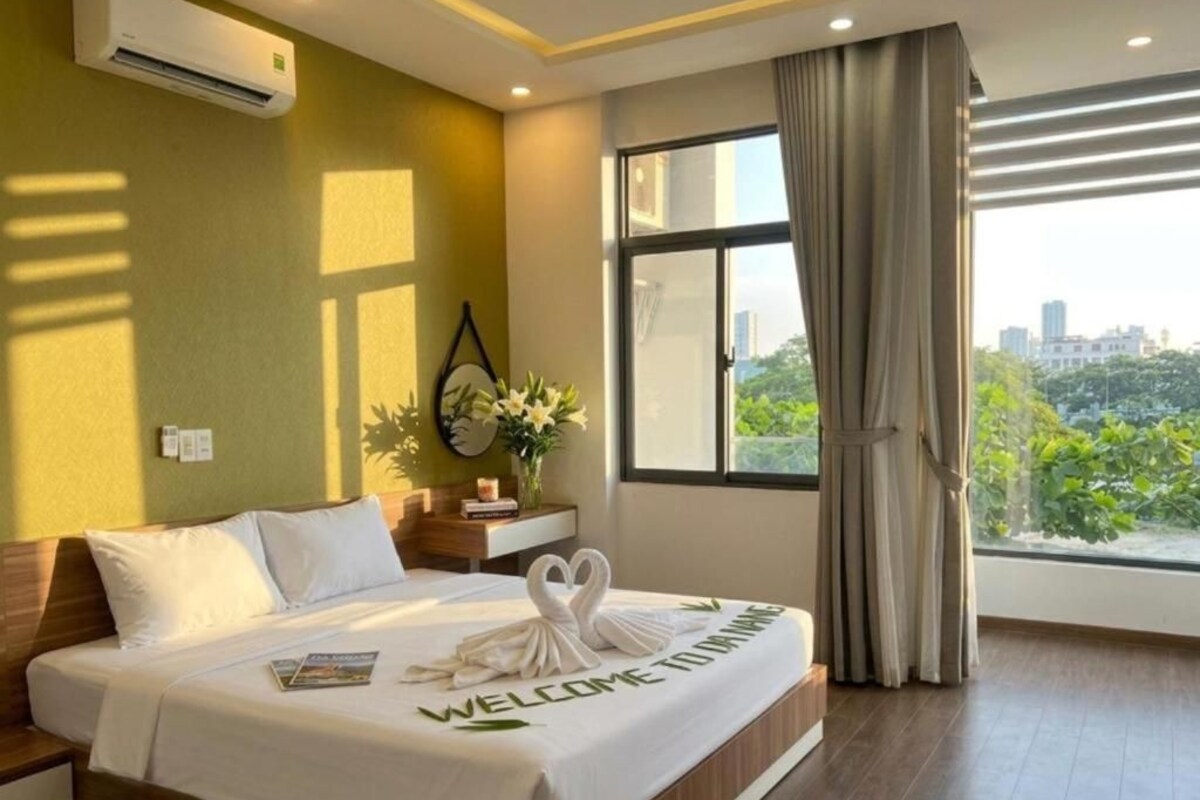 A hotel room with a bed, a nightstand, a window with curtains, and a view of the city.