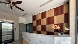 A reception desk with a marble top, a wooden panel wall, an elevator, and a ceiling fan. - JBAY Riverfront Boutique Hotel (Da Nang)