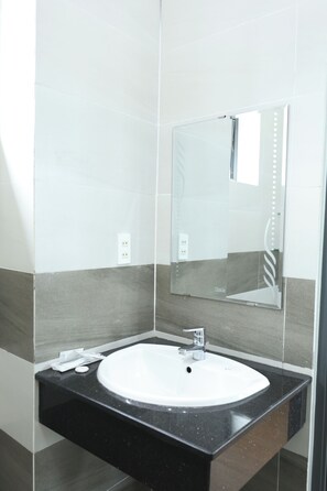 A bathroom with a white sink, a mirror, and a black countertop. - JBAY Riverfront Boutique Hotel (Da Nang)