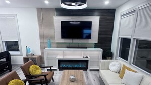 Ein modernes Wohnzimmer mit einem Flachbildfernseher, einem Kamin, einer Couch und zwei Sesseln.