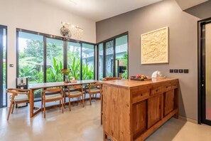 A modern kitchen with a wooden island, large windows, and a chandelier. - Chakola Villa (Ubud)