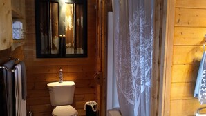Un baño rústico en una cabaña de madera, con inodoro, lavabo y cortina de ducha.