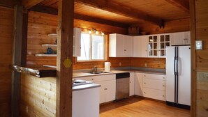 Interior de una cabaña de madera con zona de cocina, que incluye armarios, un lavamanos, una estufa y un refrigerador.