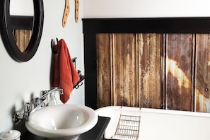 Un baño con lavamanos blanco, un espejo y una ventana con marco de madera.
