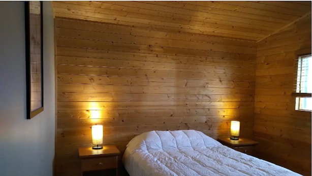 Habitación con paneles de madera, una cama, dos lámparas de noche y un ventanal.