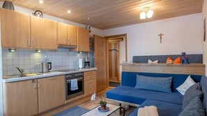 Ett kompakt kök med träskåp, en inbyggd ugn och en blå soffa med kuddar.