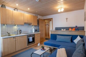 A compact kitchen with wooden cabinets, a built-in oven, and a blue sofa in the living area. - Apartment no. 3, 1-2 persons, 39 sqm, balcony and terrace, TV, WLAN (Ramsau bei Berchtesgaden)