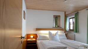 Ett hotellrum med två sängar, ett nattduksbord med en lampa, ett träpanelat tak och ett fönster med gröna gardiner.