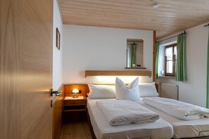 A room with two beds, a nightstand with a lamp, a window with curtains, and a wooden ceiling. - Apartment no. 3, 1-2 persons, 39 sqm, balcony and terrace, TV, WLAN (Ramsau bei Berchtesgaden)