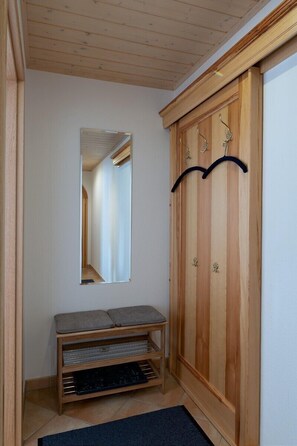 En hall med en träbänk, en spegel och en garderob med krokar.
