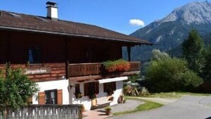 En traditionell byggnad i chalet-stil med en träfasad, en balkong med växter och en bergskedja i bakgrunden.