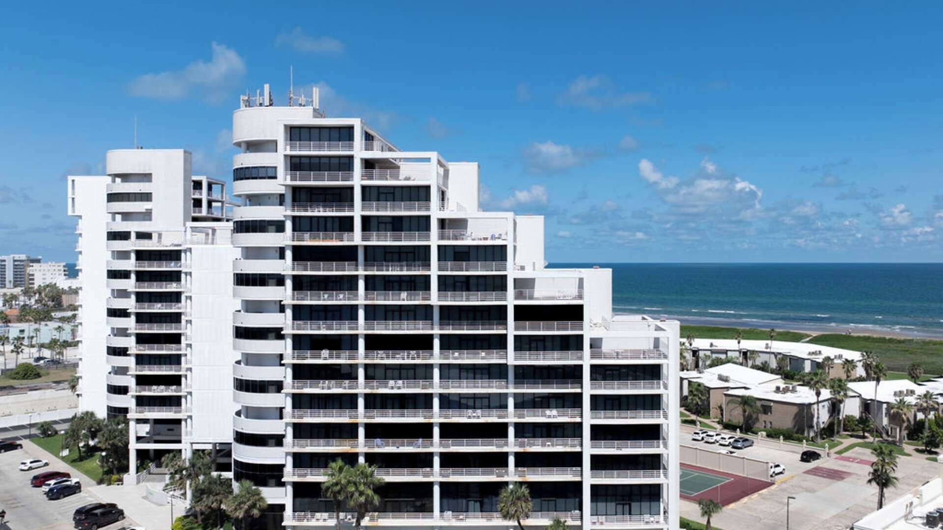 Un hotel de varios pisos con balcones, un estacionamiento y vista al océano.