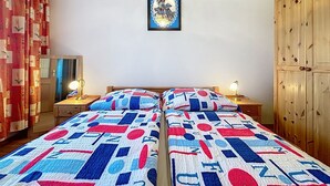 Ein Schlafzimmer mit zwei Betten, einem Holzschrank, einem gerahmten Bild an der Wand und einem Spiegel links an der Wand.