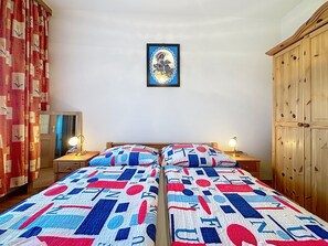 Ein Schlafzimmer mit zwei Betten, einem Holzschrank, einem gerahmten Bild an der Wand und einem Spiegel links an der Wand.