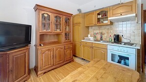A compact kitchen with wooden cabinets, a built-in oven, a dining table, and a flat-screen TV. - Apartment Ivo by Interhome (Pula/Banjole)
