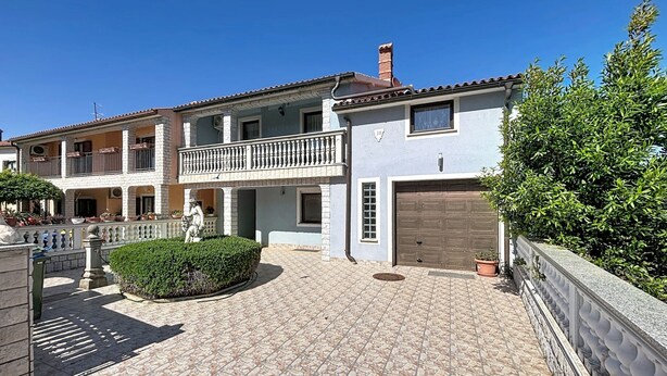 Ein zweistöckiges Gebäude mit Balkon, Garage und gepflastertem Innenhof.