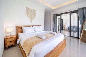 A modern hotel room with a large bed, a nightstand, a wall hanging, and a view through a glass door. - Gauri Villa (Gianyar)
