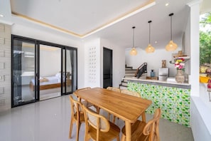 A modern kitchen with a dining area, a staircase, and a view of a bedroom. - Gauri Villa (Gianyar)
