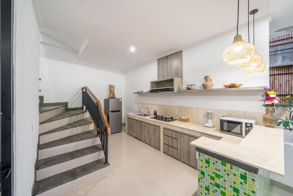 Une cuisine moderne avec un escalier, des meubles en bois, un four à micro-ondes et un luminaire suspendu.