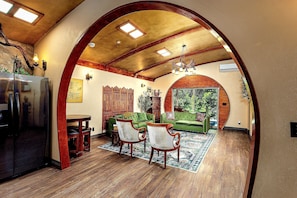 An interior with a wooden ceiling, a dining area with chairs and a table, and a green sofa.