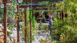 Een tuin met een houten pergola, hangende glazen potten en verschillende planten.