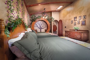 Une chambre à coucher avec un grand lit, une commode en bois, une décoration murale représentant un arbre et une porte circulaire en bois.